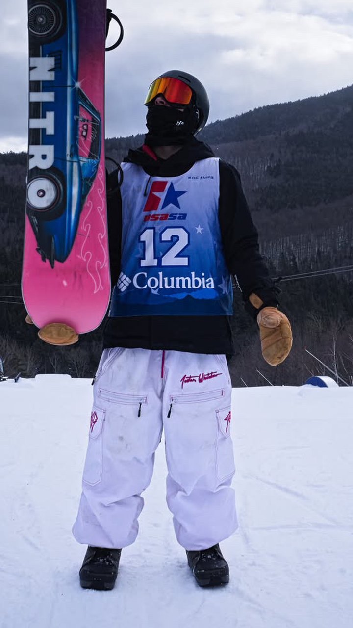 Snowboarder holding his board in white Trashbags snow pants